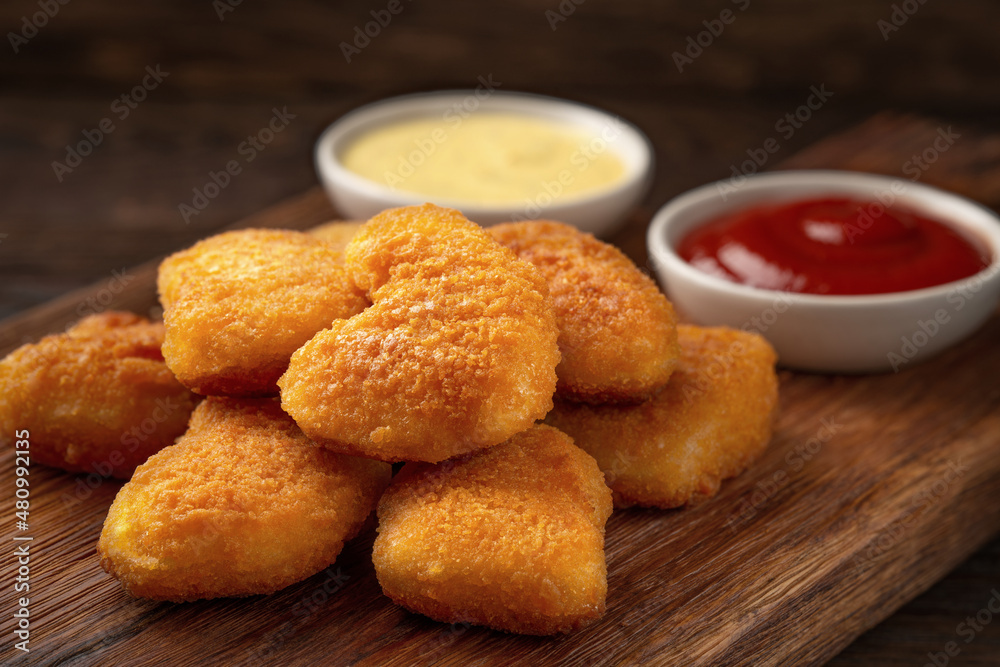 Homemade chicken nuggets and sauces on a cutting board close-up Homemade chicken nuggets and sauces on a cutting board close-up