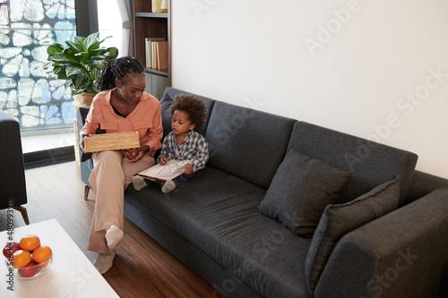 Mother spending time with little son drawing picture when sitting on sofa at home
