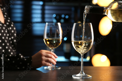 Pouring white wine from bottle into glass on bar counter