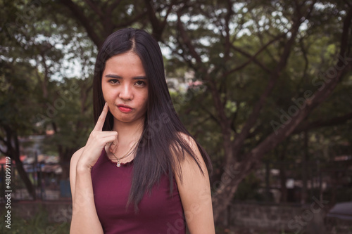Fotografia A doubtful and skeptical Filipina woman in a maroon sleeveless blouse at the park