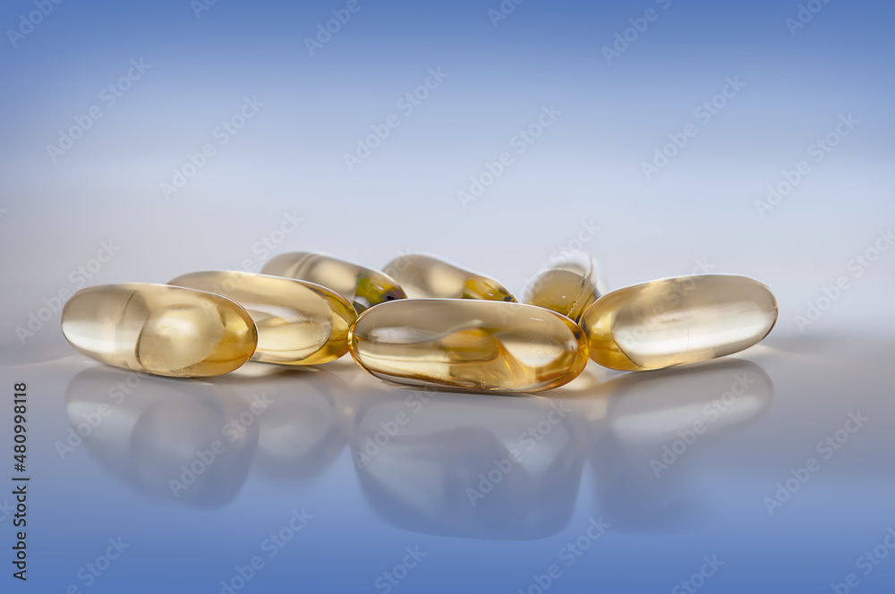 yellow vitamin e fish oil capsule on light blue background with reflection close up yellow vitamin e fish oil capsule on light blue background with reflection close up