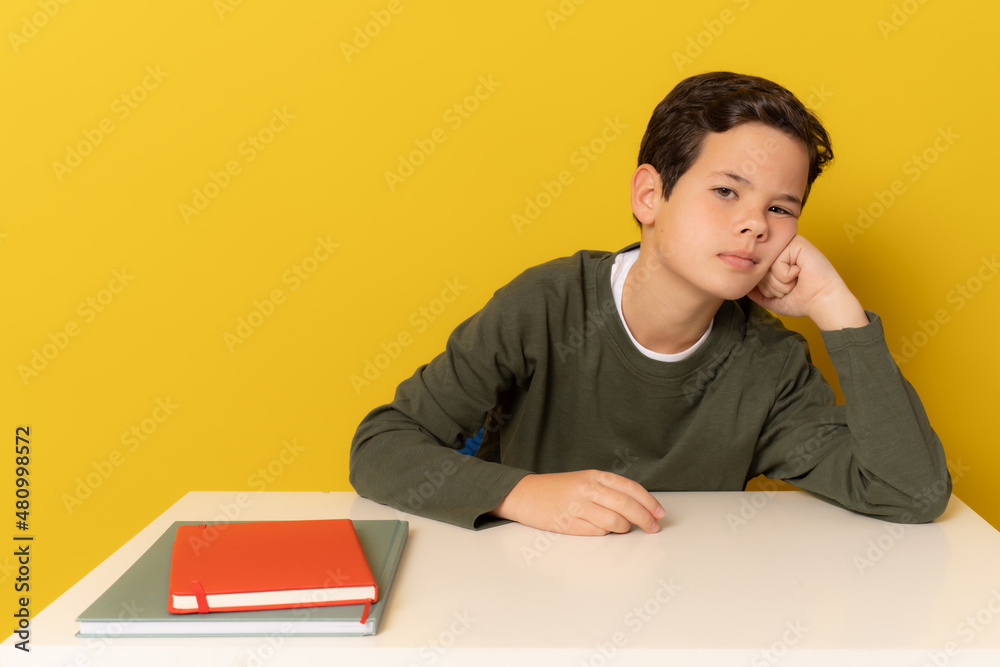 Student bored boy sitting on the desk isolated over yellow background.