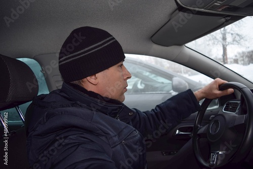 A young man in warm clothes is driving a car