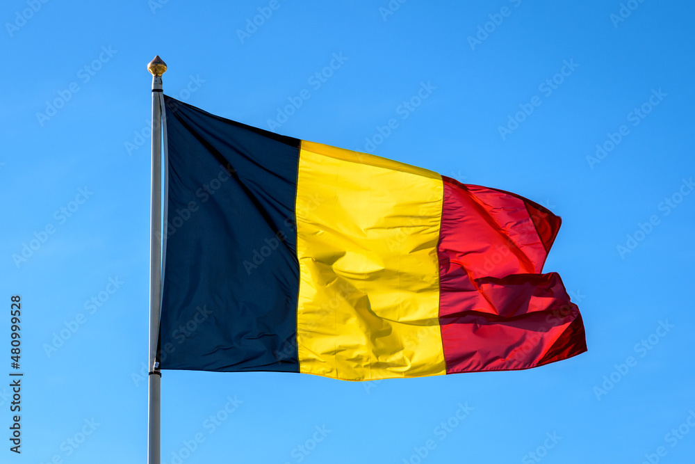 The national flag of Belgium is flying in the wind at full mast against blue sky. The national flag of Belgium is flying in the wind at full mast against blue sky.