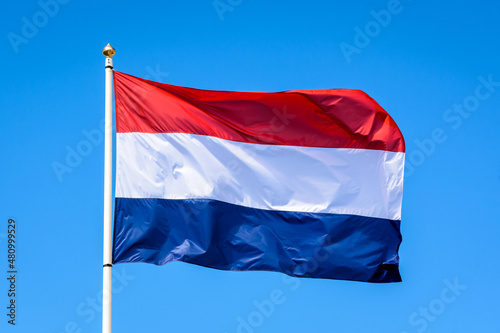 The national flag of the Netherlands is flying in the wind at full mast against blue sky.