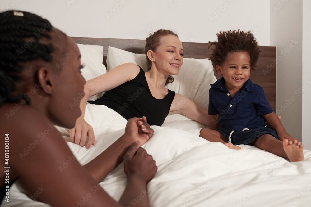 Boy with strabismus sitting in bed with his two mothers and watching movie or animated cartoon Boy with strabismus sitting in bed with his two mothers and watching movie or animated cartoon