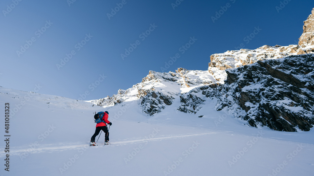 A skier is walking up the hill. Skitouring in Alps. Sunny weather. Adventure winter sport