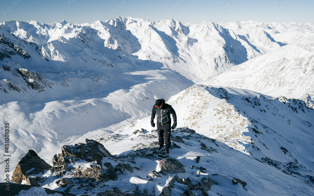 Climber on top of a mountain in the background of a landscape of snowy mountains. Alps range tourism.  Winter vacations, active lifestyle, skiing and trekking concept.