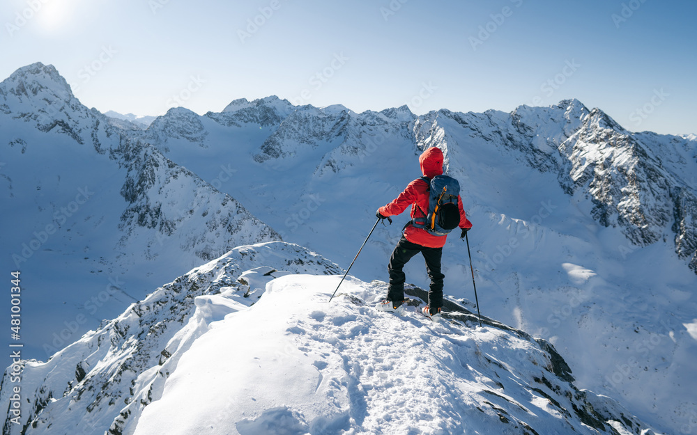Climber on top of a mountain in the background of a landscape of snowy mountains. Alps range tourism.  Winter vacations, active lifestyle, skiing and trekking concept.