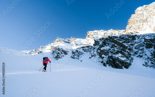 A skier is walking up the hill. Skitouring in Alps. Sunny weather. Adventure winter sport