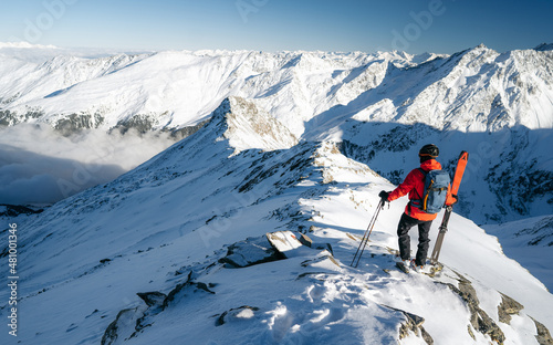 Climber on top of a mountain in the background of a landscape of snowy mountains. Alps range tourism. Winter vacations, active lifestyle, skiing and trekking concept.