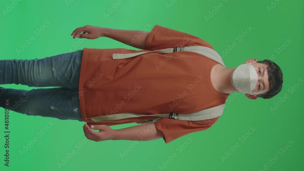 The Front View Of Asian Boy Student Wearing A Mask, Backpack, Brown T-Shirt, And Blue Jeans Walking To School On Green Screen Chroma Key.
