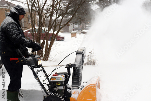 senior man snow blowing driveway during storm.