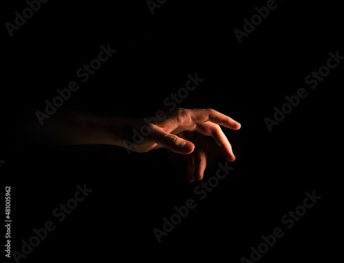 Male hand reaches for the light in the dark on an isolated black background. Side view 