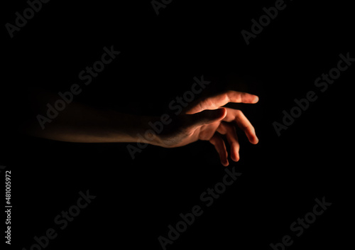 Male hand reaches for the light in the dark on an isolated black background. Side view 
