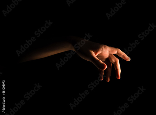 Male hand reaches for the light in the dark on an isolated black background. Side view 