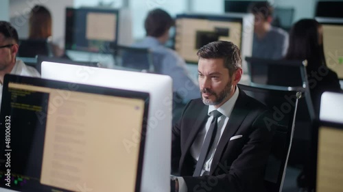 Serious Adult Bearded Man Working on Decktop Computer While Working in Big Open Space Office. Portrait of Positive Business Man Looking at Computer Screen Indoors. photo