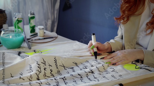 Close-up of a beautiful red-haired girl drawing with multicolored paints on clothes. Handmade work