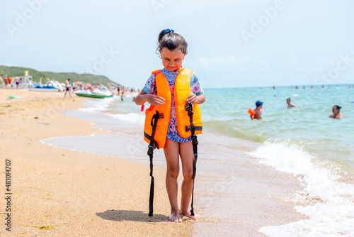 Little happy girl in a life jacket during a walk on the seashore. The concept of a safe holiday. Summer holidays 