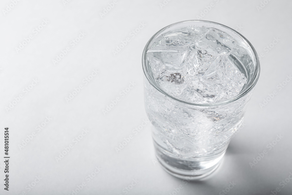 Glass of soda water with ice on light background. Space for text Glass of soda water with ice on light background. Space for text