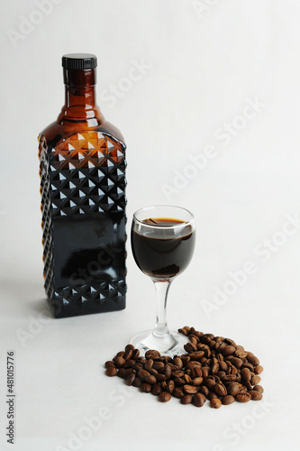 Coffee liqueur in dark glass bottle and poured into a glass. White background, scattered coffee beans