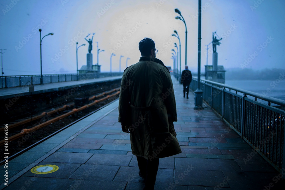 Back of cinematic young man in winter coat walking outside in urban