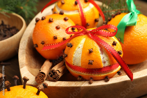 Pomander balls with ribbons made of fresh tangerines and cloves in wooden plate, closeup photo