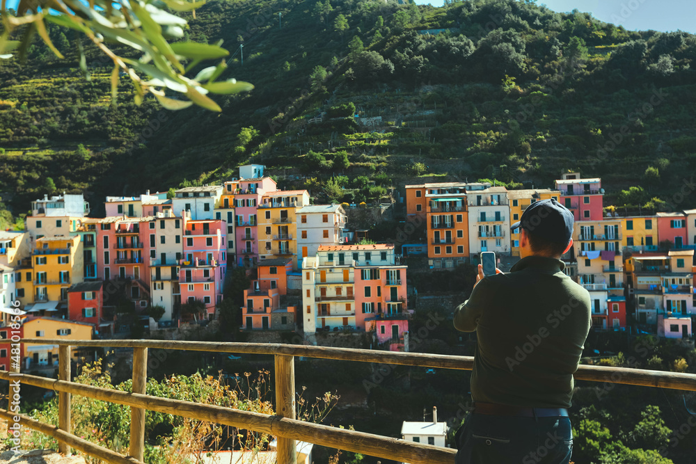 Selective focus on mobile phone, ataking photo at panoramic view of Riomaggiore colorful village, Cinque Terre, Italy - obrazy, fototapety, plakaty 