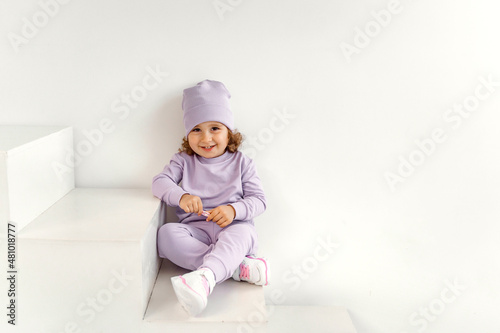 a little girl in a purple suit and hat on a light background is playing