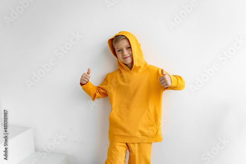 a teenager in a yellow tracksuit on a monochrome background in a hood shows super photo