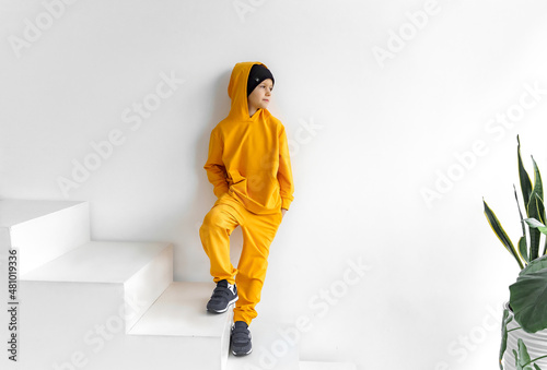 a teenage boy in a yellow tracksuit, wearing a hood looks away