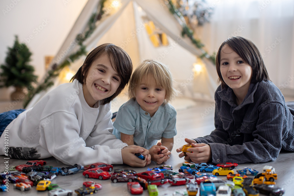 Cute toddler child and his older brothers, playing with colofrul cars, different sizes and colors on the floor