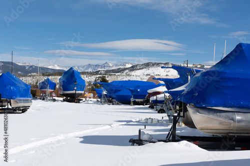 Boats are wrapped and stored for the winter with mountains in the background in Frisco, Colorado with snow on ground.