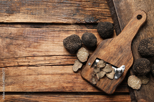 Shaver with whole and sliced black truffles on wooden table, flat lay. Space for text photo