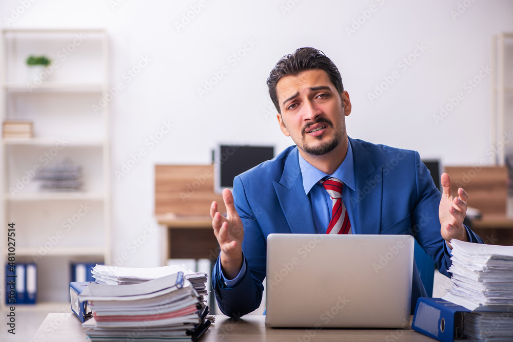 Young male employee unhappy with excessive work at workplace Young male employee unhappy with excessive work at workplace
