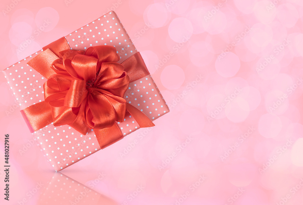 Pink gift box with a red bow on a pink background with bokeh and reflection. Close-up. Pink gift box with a red bow on a pink background with bokeh and reflection. Close-up.