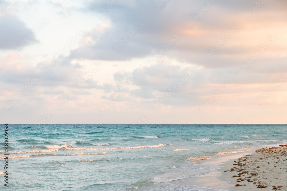 Fototapeta premium Gentle Sunrise on the coast of the Atlantic Ocean. Seascape with turquoise waves of the sea, pink hues on a sunset on a tourist beach. Relaxing holidays by the sea at the magical sunset of Varadero
