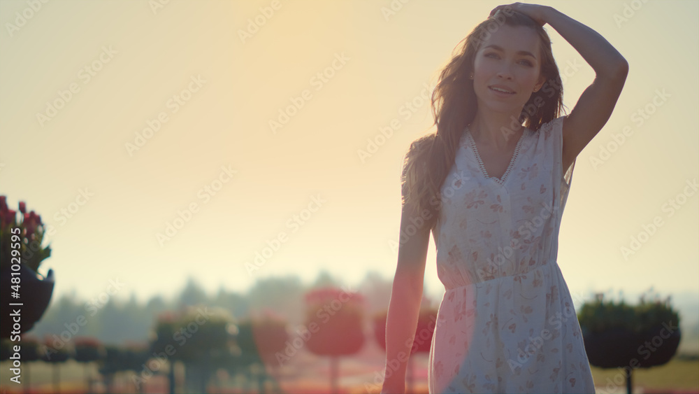 Smiling woman walking in garden. Emotional girl touching hair in sun reflection.
