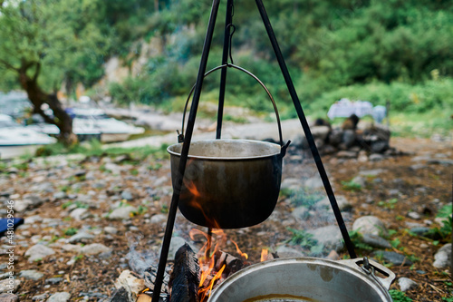 Bowler cooking food bonfire cauldron camp fire, pot. Hiking pot in the bonfire. Traveling in the mountains with tents. photo