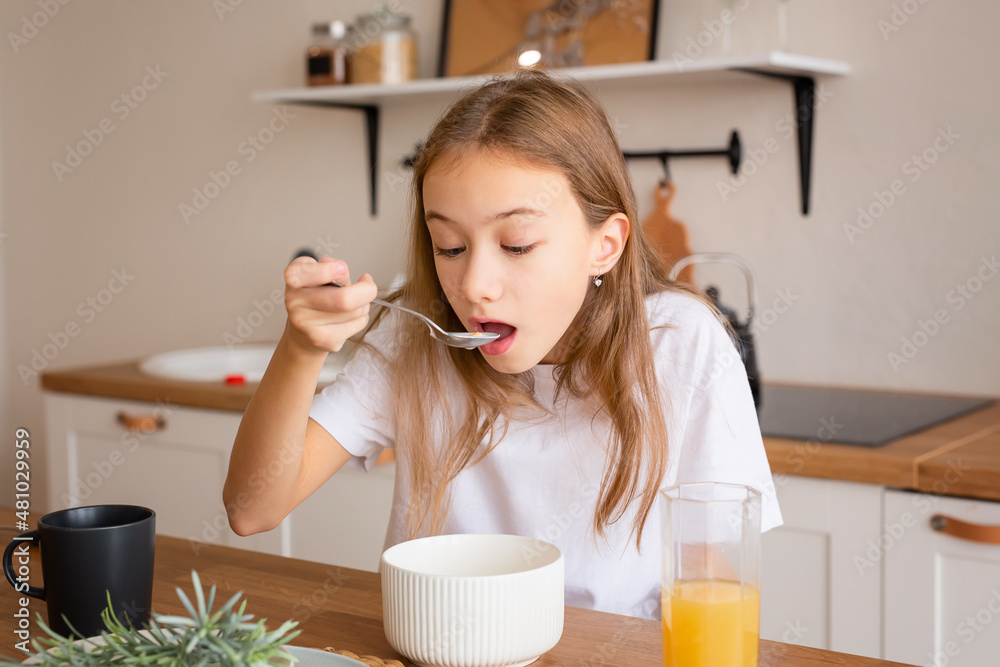 A cute girl is having breakfast at home. A girl eats healthy food in the morning while sitting in a modern kitchen A cute girl is having breakfast at home. A girl eats healthy food in the morning while sitting in a modern kitchen