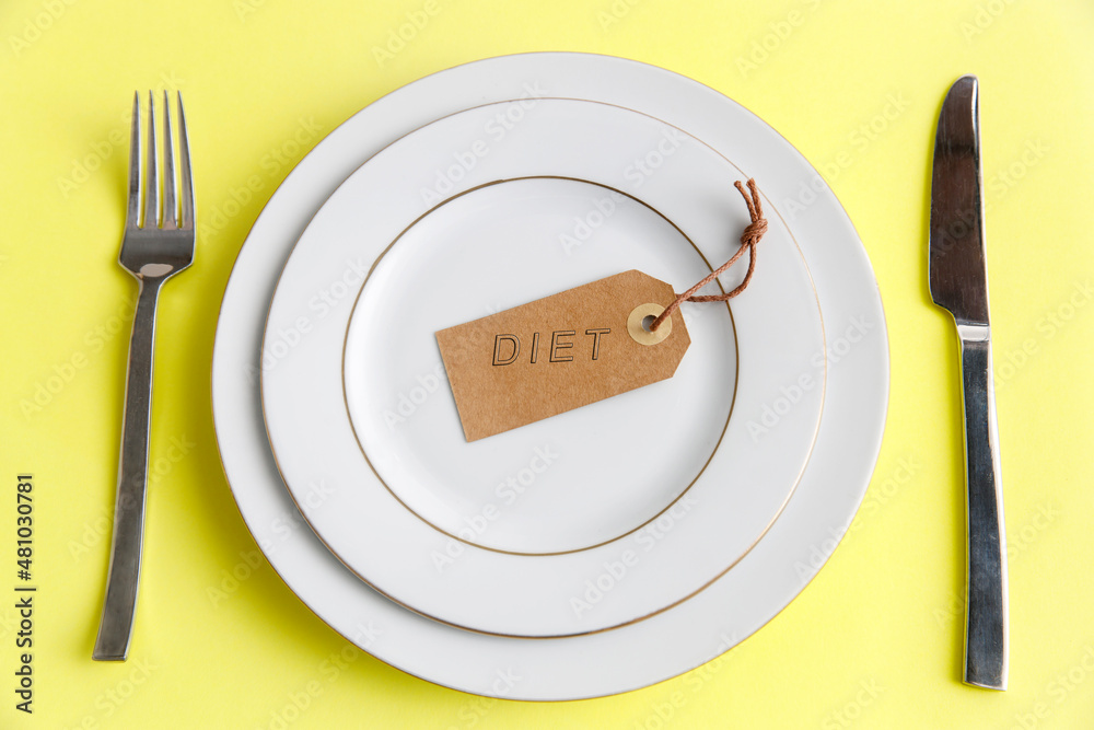 Serving two plates, spoon, fork, knife on the yellow background. The concept of weight loss and diet. The concept of weight loss and diet. Label with the inscription - diet in an empty plate Serving two plates, spoon, fork, knife on the yellow background. The concept of weight loss and diet. The concept of weight loss and diet. Label with the inscription - diet in an empty plate