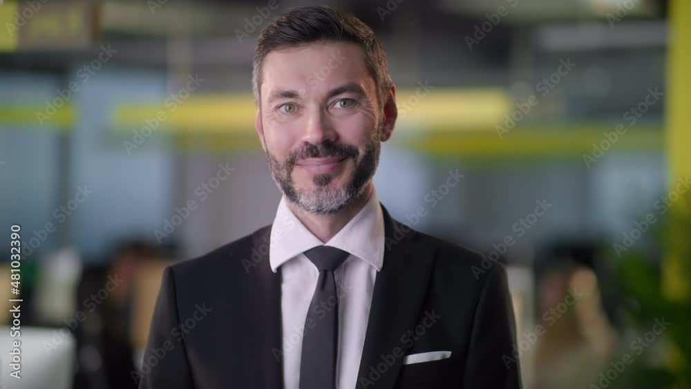 Front view of portrait of professional businessman in suit looking to camera and smiling at coworking zone. Young startup founder looking happy and standing at office room. Front view of portrait of professional businessman in suit looking to camera and smiling at coworking zone. Young startup founder looking happy and standing at office room.