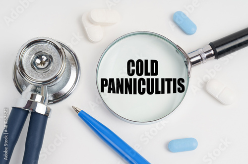 On a white surface lie pills, a pen, a stethoscope and a magnifying glass with the inscription - Cold panniculitis photo