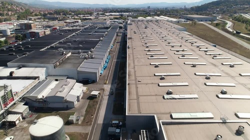 Big factory warehouse rooftop. Aerial drone shot camera flying forward. Factory rooftop, roof windows, ventilation shafts, flat roof of a big factory warehouse. Aerial drone shot camera parallel