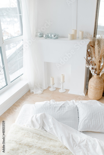 A white bed and a white decorative fireplace. Cozy bright bedroom in minimalism style. Minimalistic trendy interior.