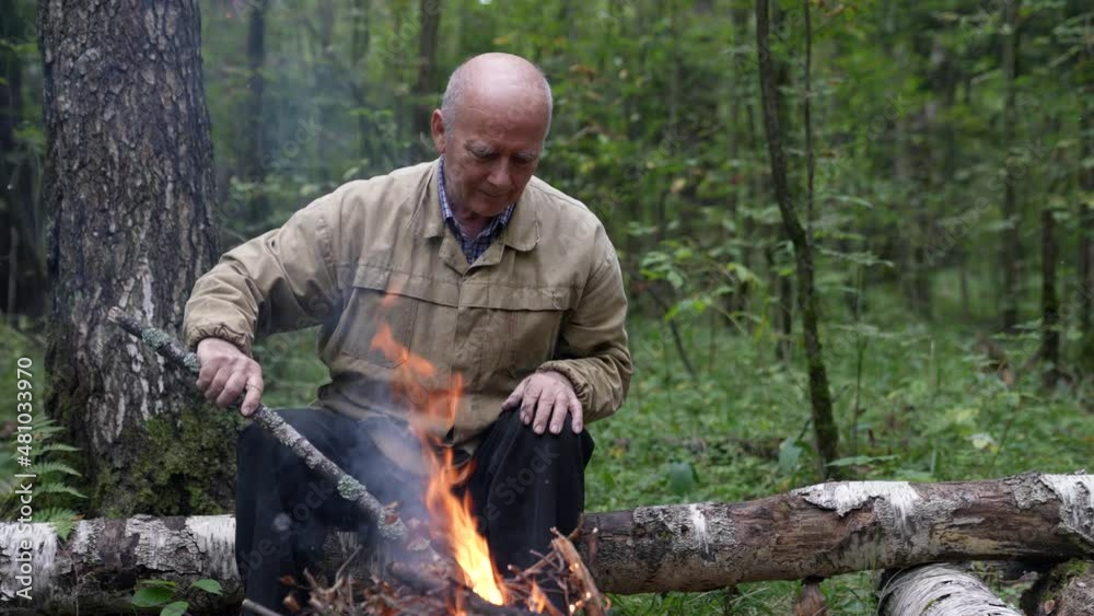 A man at a campfire in the forest. An old man looks at a forest fire in nature in summer. A lonely traveler is sitting and resting by the campfire A man at a campfire in the forest. An old man looks at a forest fire in nature in summer. A lonely traveler is sitting and resting by the campfire