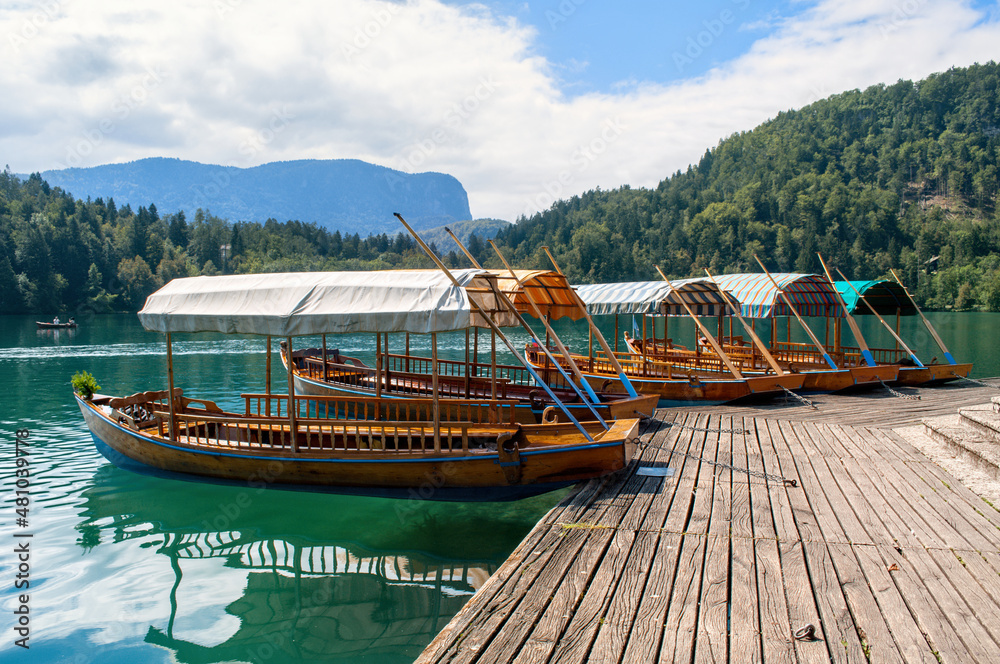 Small wooden boats park in the harbor at the wooden pier on Lake Bled in the Slovenian mountains.