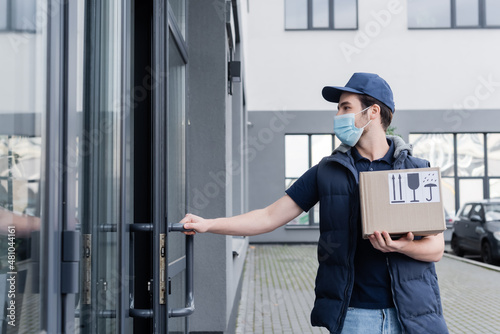 Wallpaper Mural Delivery man in uniform and protective mask holding carton box and opening door of building outdoors. Torontodigital.ca