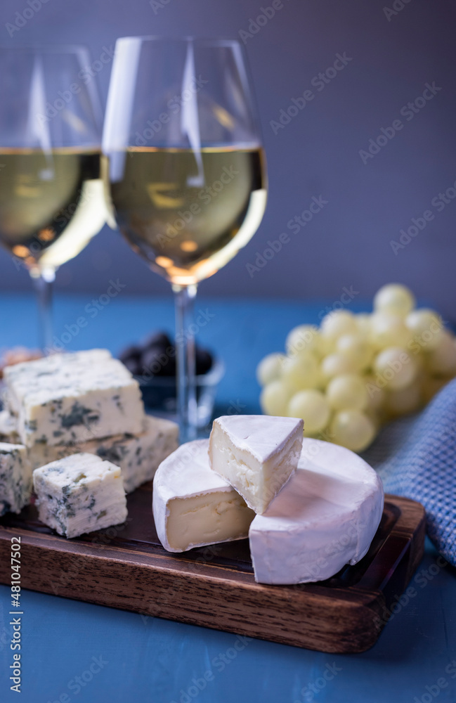 an appetizer assorted dor blue cheese and camembert on a wooden board with honey and grapes and with glasses of wine on a blue background an appetizer assorted dor blue cheese and camembert on a wooden board with honey and grapes and with glasses of wine on a blue background