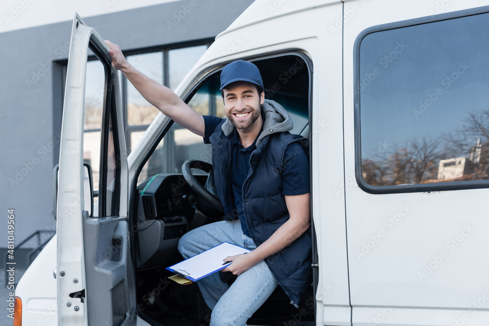 happy delivery man looking at camera while holding clipboard and parcel in auto. happy delivery man looking at camera while holding clipboard and parcel in auto.